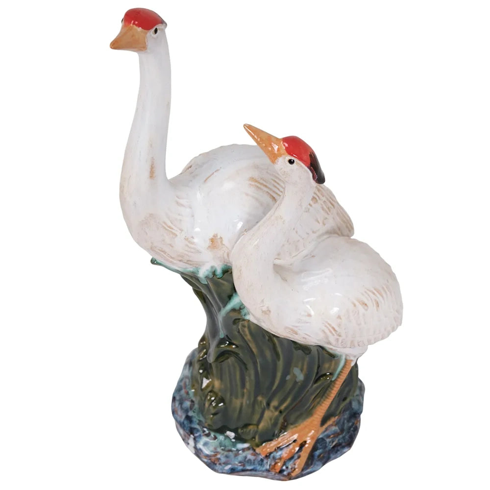Front view of a white ceramic crane figurine with red crowns, standing together in a green marsh base.