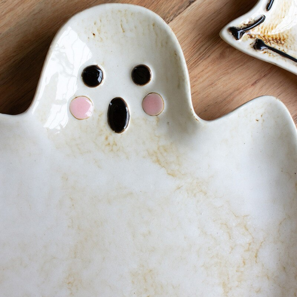 Ghost-shaped ceramic serving platter with a cute face on a wooden background.