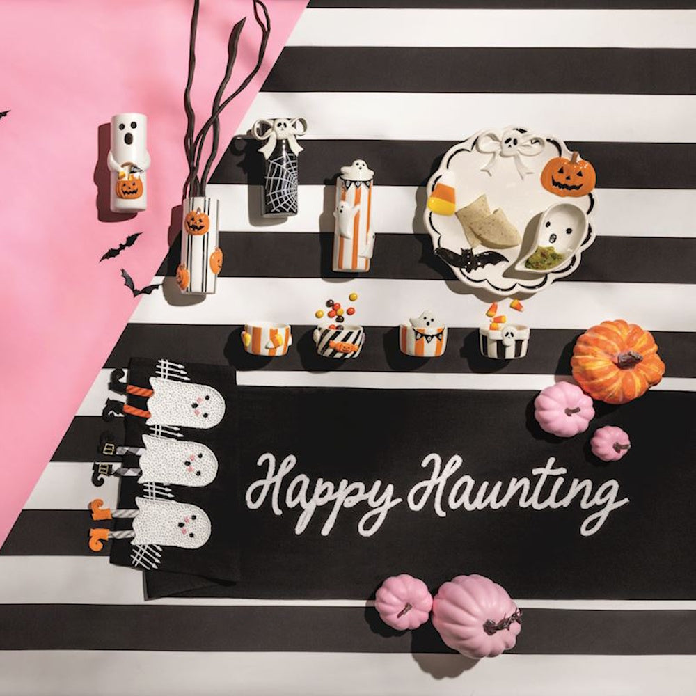 Halloween table runner with "Happy Haunting" text and cute ghost details amid themed decor.