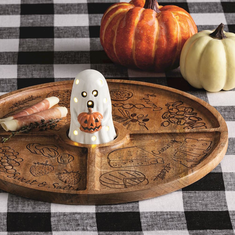 Light-up ceramic ghost holding a pumpkin on a wooden charcuterie board with Halloween pumpkins behind it.
