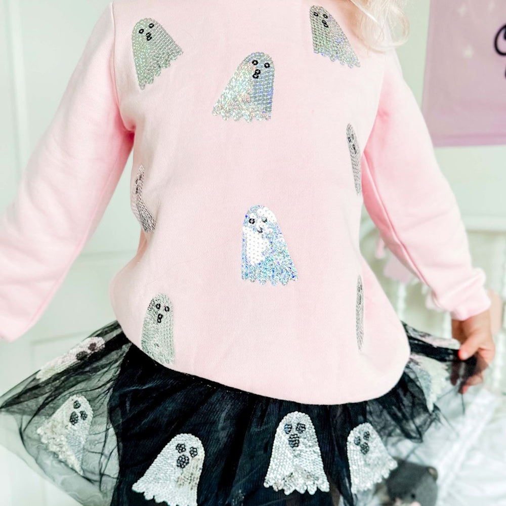 Child wearing a pink sweatshirt and black tulle skirt, both decorated with sequined Halloween ghosts.