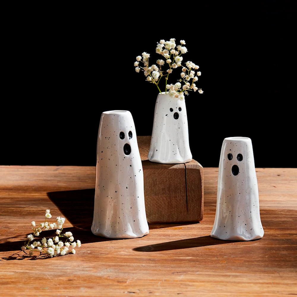 Three ceramic ghost vases with baby's breath flowers on a wooden table.