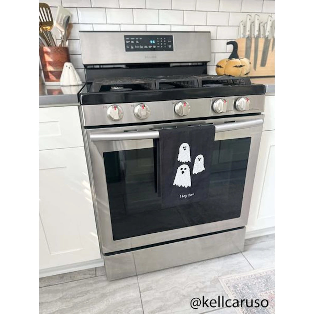 Black Halloween ghost towel hanging on a stainless steel oven handle in a modern kitchen.