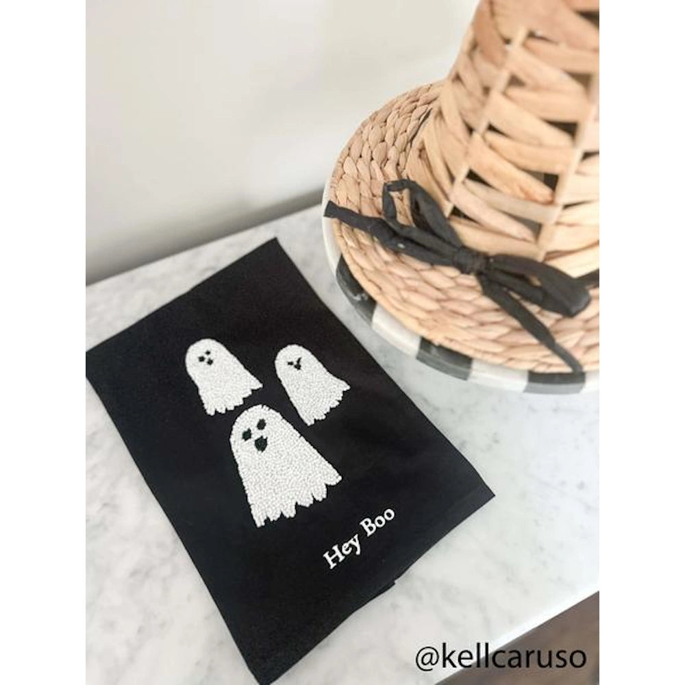 Black Hey Boo ghost dish towel neatly folded on a white marble countertop next to Halloween decor.