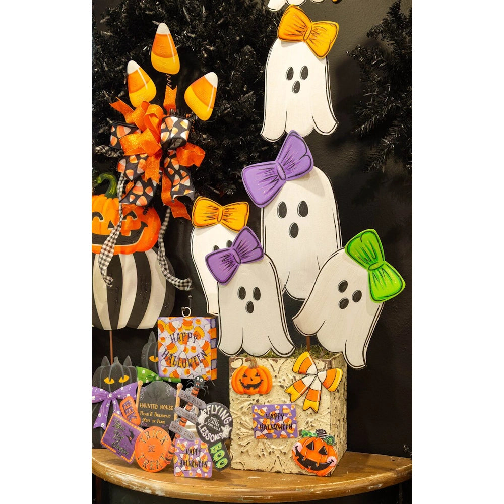 Halloween display featuring white ghost stakes with bows, a candy corn topiary, and black cat decorations.