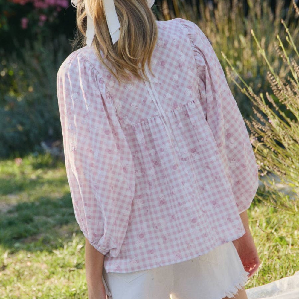 Woman wearing a pink and white floral gingham blouse and white shorts in a garden.