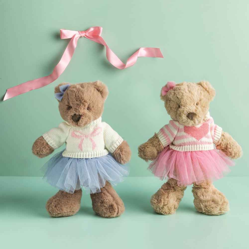 Two adorable teddy bears wearing knitted sweaters and tutus, one in blue and one in pink, against a soft green background.