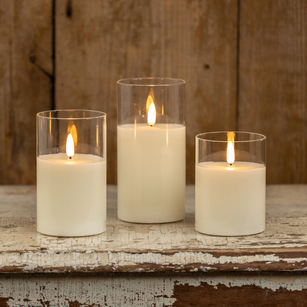 Three lit white pillar candles in clear glass cylinders on a rustic distressed wooden surface.