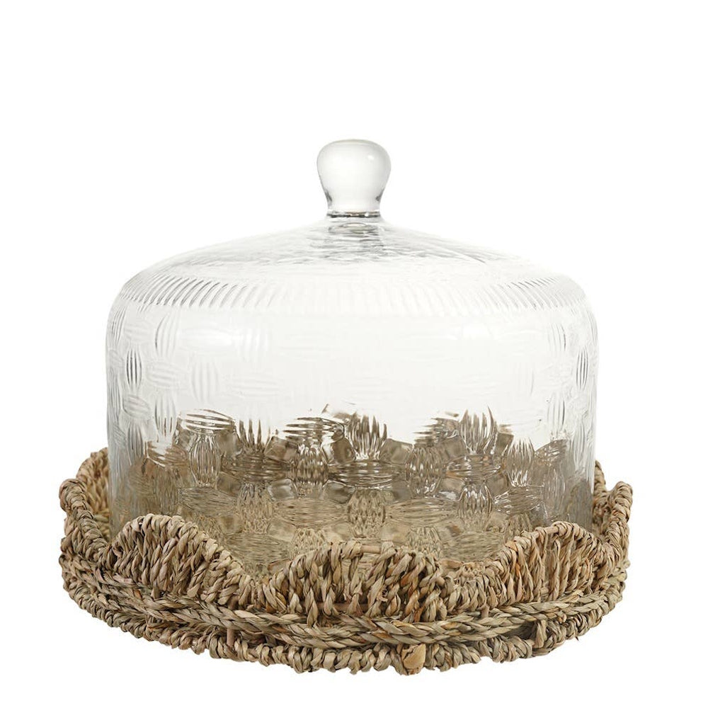 Clear patterned glass cloche dome resting inside a woven seagrass tray with scalloped edges.