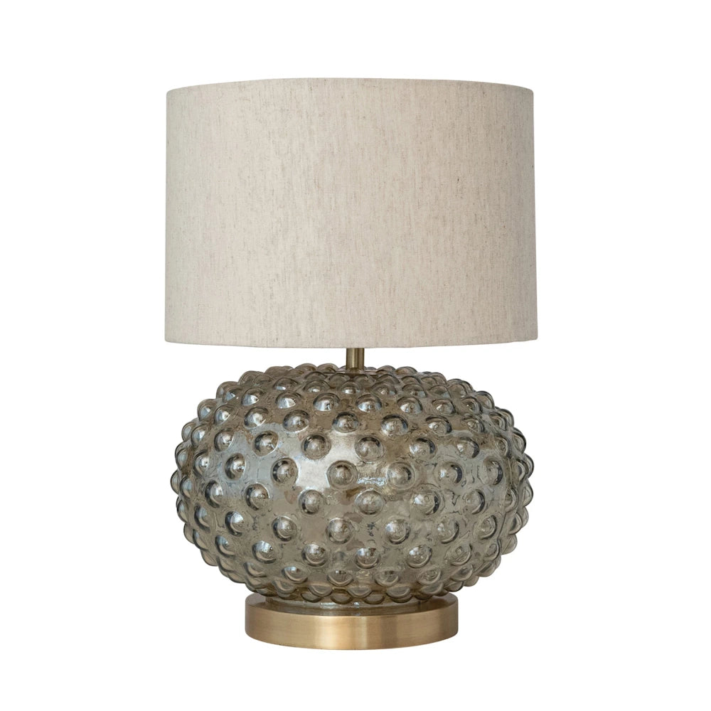 Smoky glass hobnail table lamp with brass base and cream cotton drum shade on a white background.