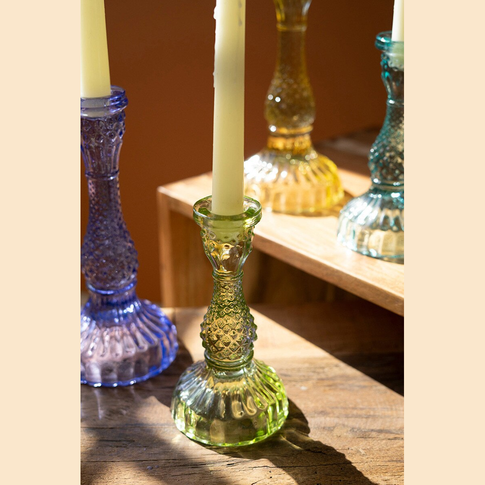 Colorful vintage-style textured glass taper candle holders in purple, green, yellow, and blue on a wooden surface.