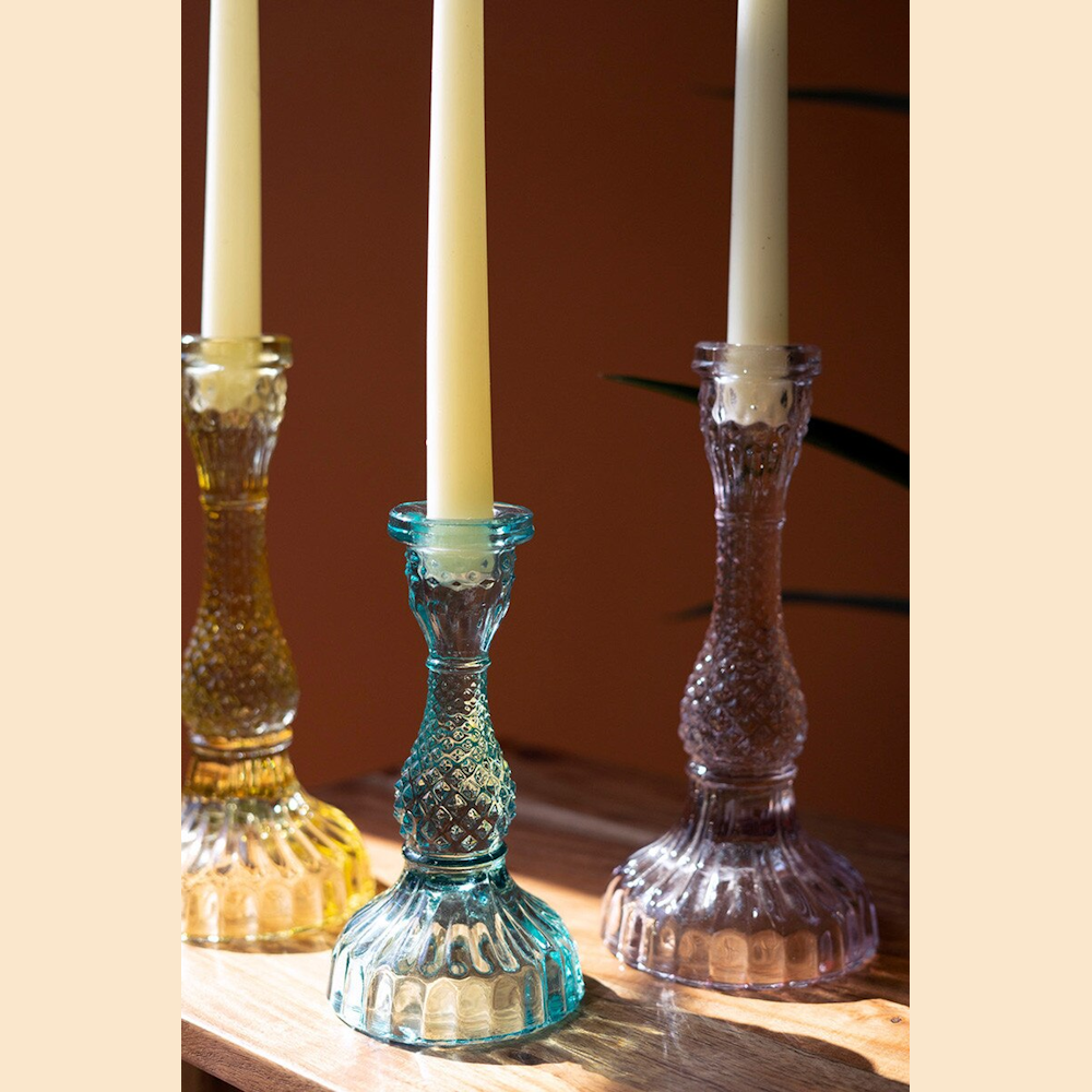 Three colorful textured glass taper candle holders in amber, teal, and lavender with white candles on a wooden surface.