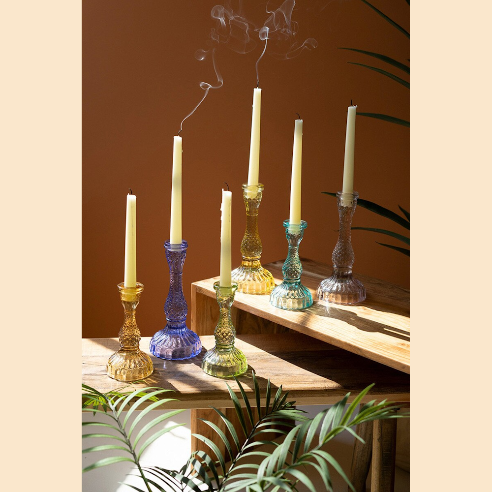 Colorful vintage-style glass taper candle holders in various jewel tones with white candles on a wooden table.