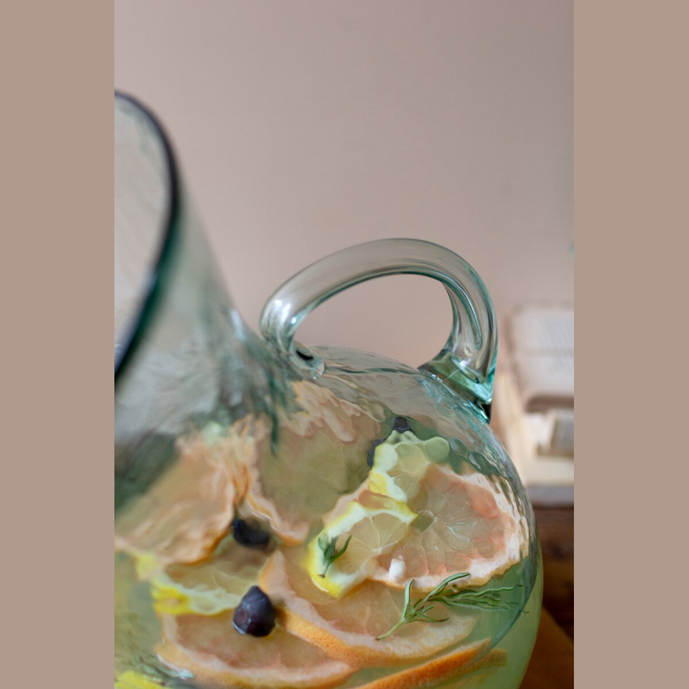 Close-up of a glass pitcher with citrus infused water, lemon slices, and rosemary sprigs for a refreshing drink.