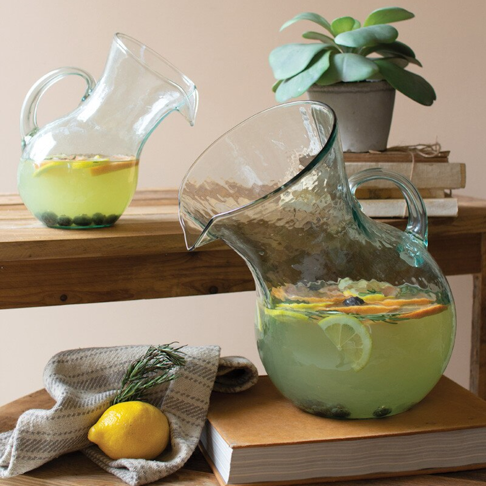 Handcrafted tilted glass pitcher filled with citrus-infused lemonade on a rustic wooden table with a lemon and books.