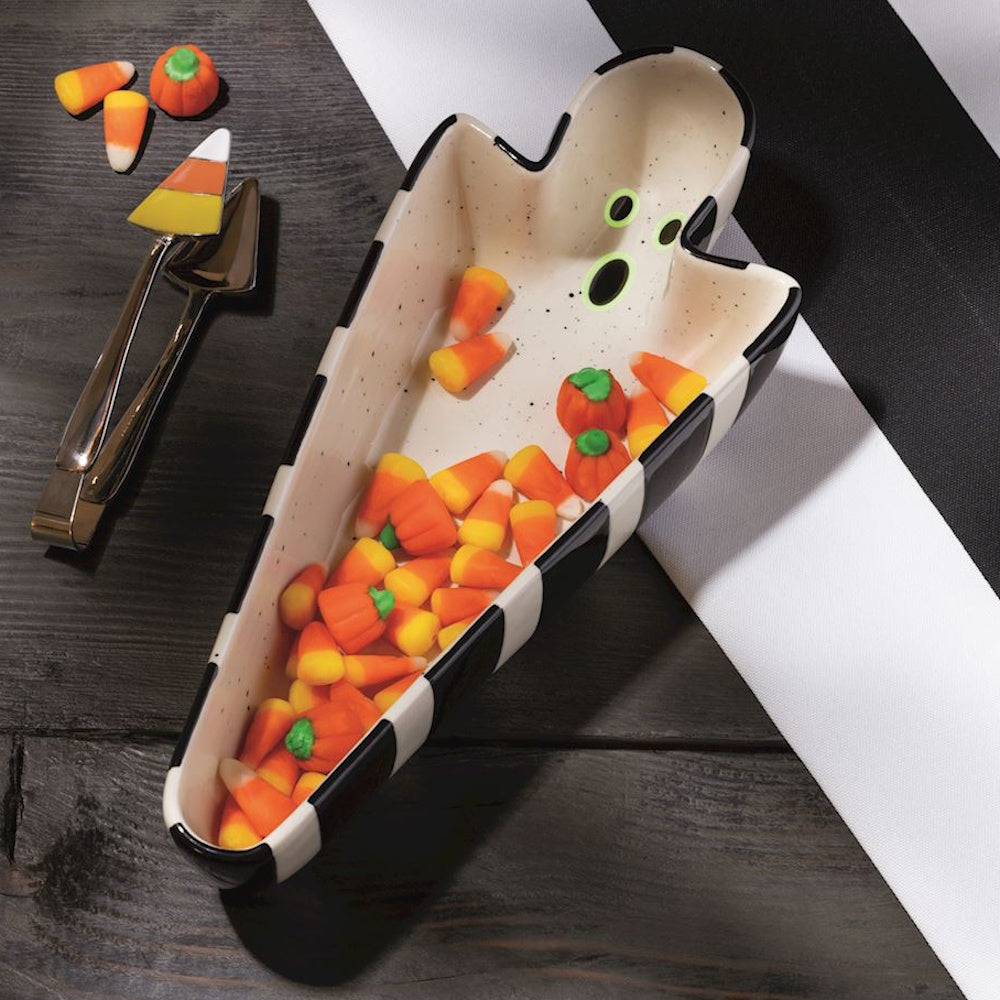 Ghost-shaped Halloween candy dish filled with candy corn and pumpkin candies on a table.