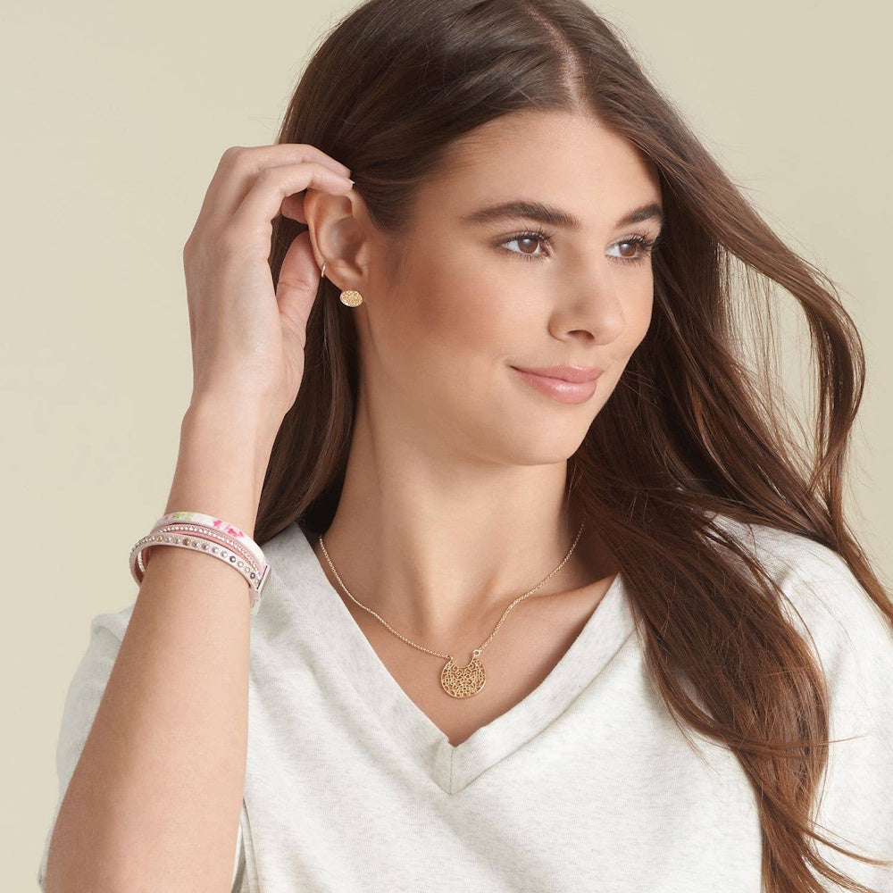 Woman wearing a gold filigree circle necklace, matching stud earrings, and pink wrap bracelets.