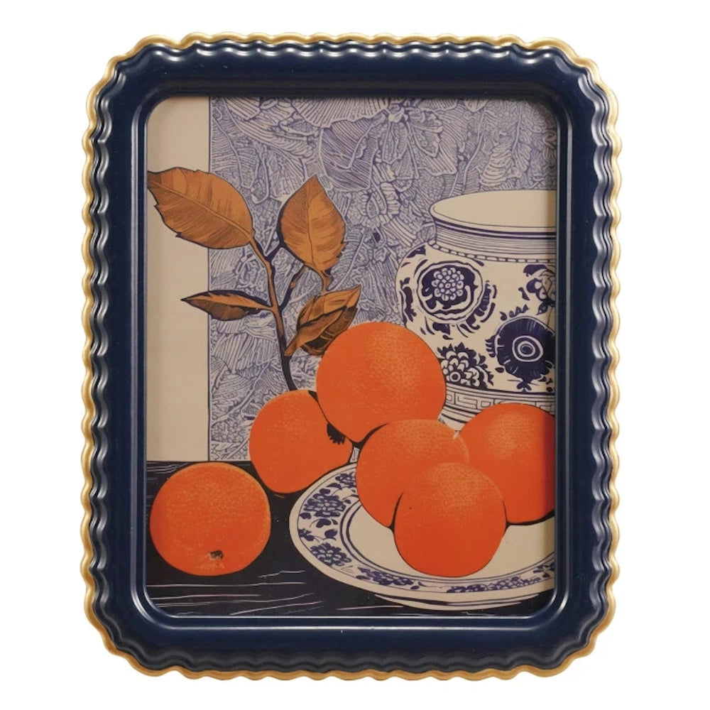 Still life art of oranges and blue patterned pottery in a navy blue scalloped frame with a gold-finish edge.