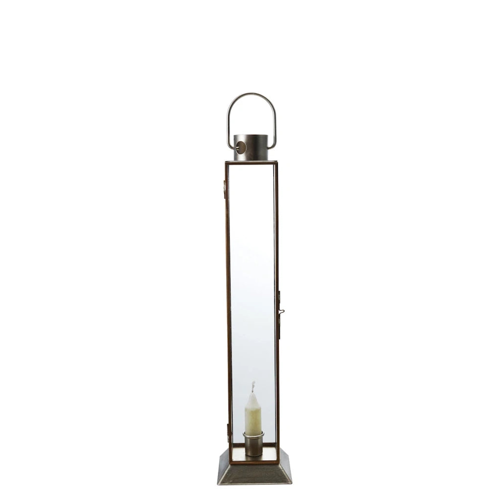 Tall gold finish metal and glass lantern with a white taper candle inside against a white background.
