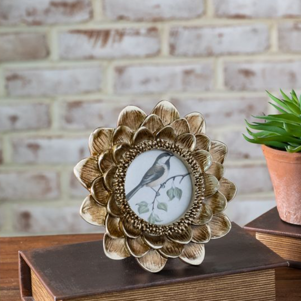 Gold flower-shaped photo frame displaying a bird illustration resting on a book.