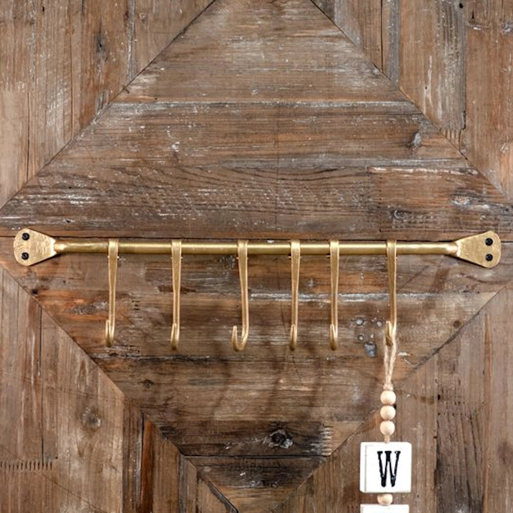 Gold iron wall-mounted rail with six hooks, fixed to a rustic diamond-patterned wood backdrop.