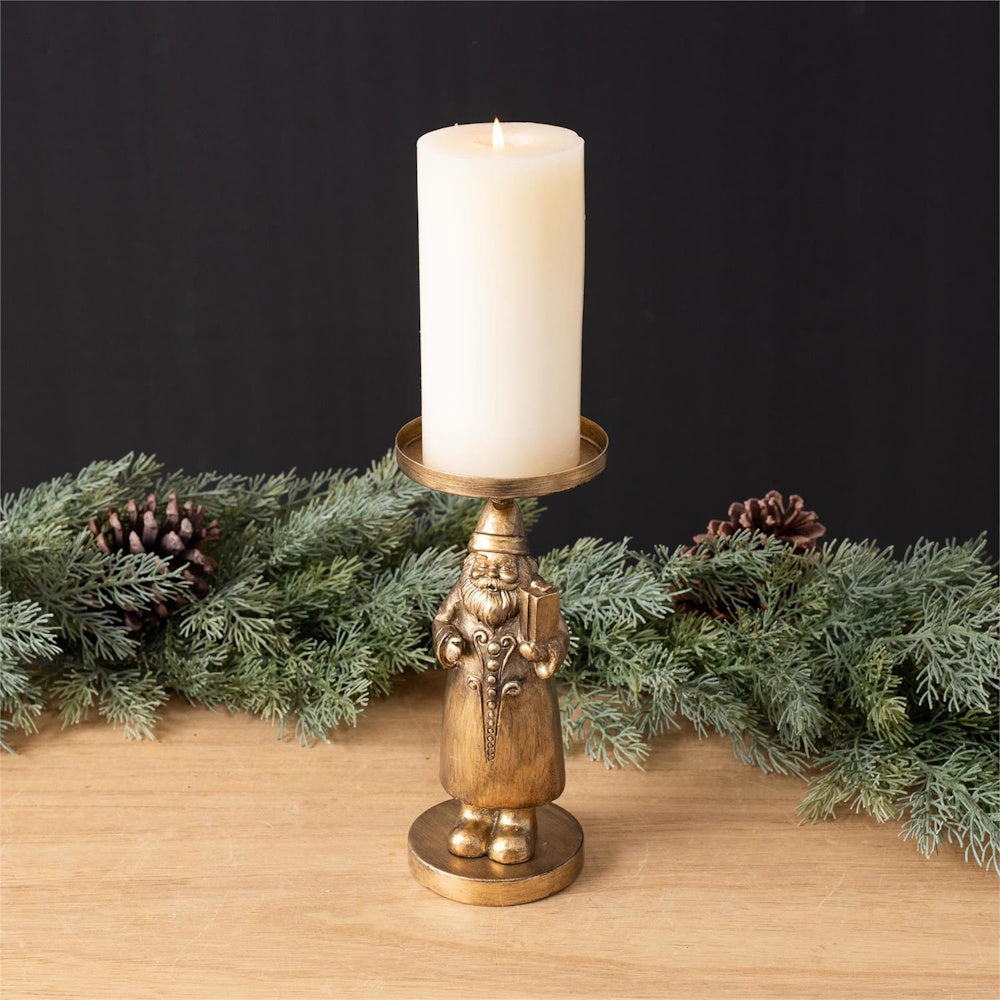 Gold Santa candle holder with a white pillar candle on a wooden table before pine garland.