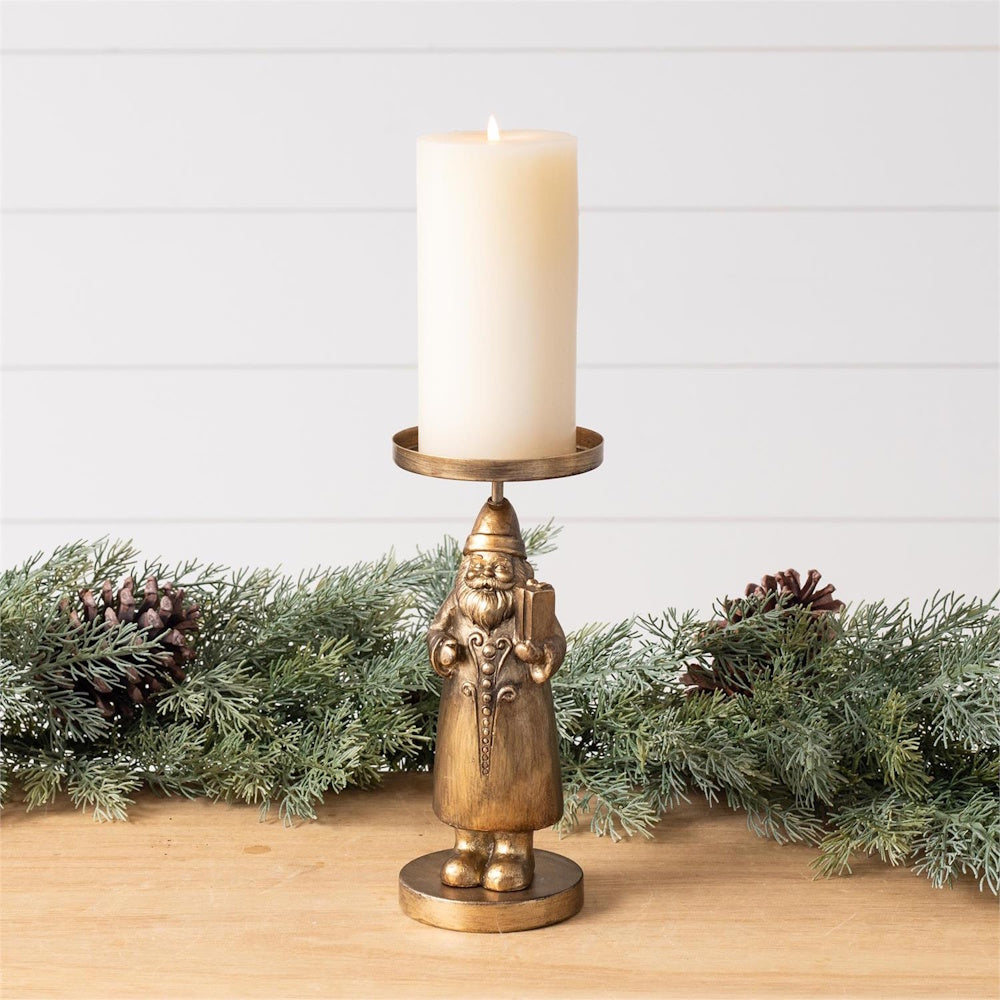 Gold Santa Claus candle holder holding a pillar candle, set on a wooden surface with pine garland.