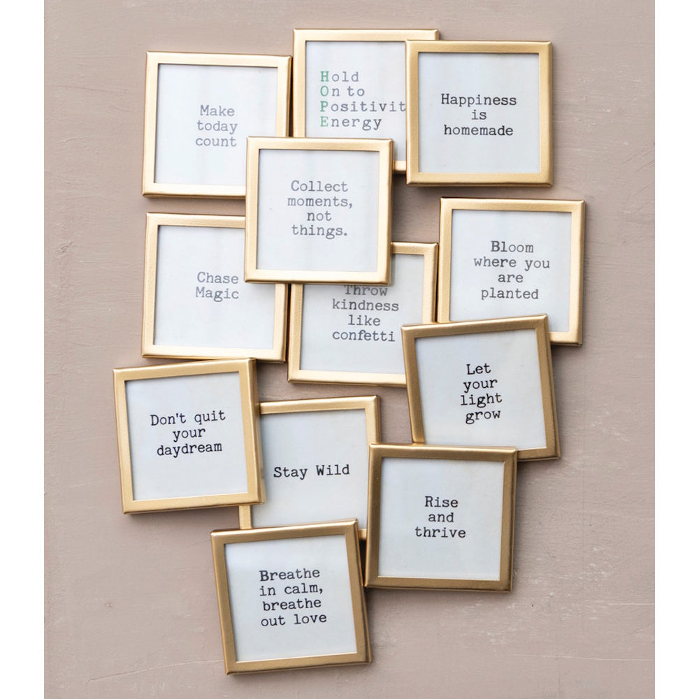 A collection of square gold metal-framed glass magnets with motivational sayings arranged on a wall.