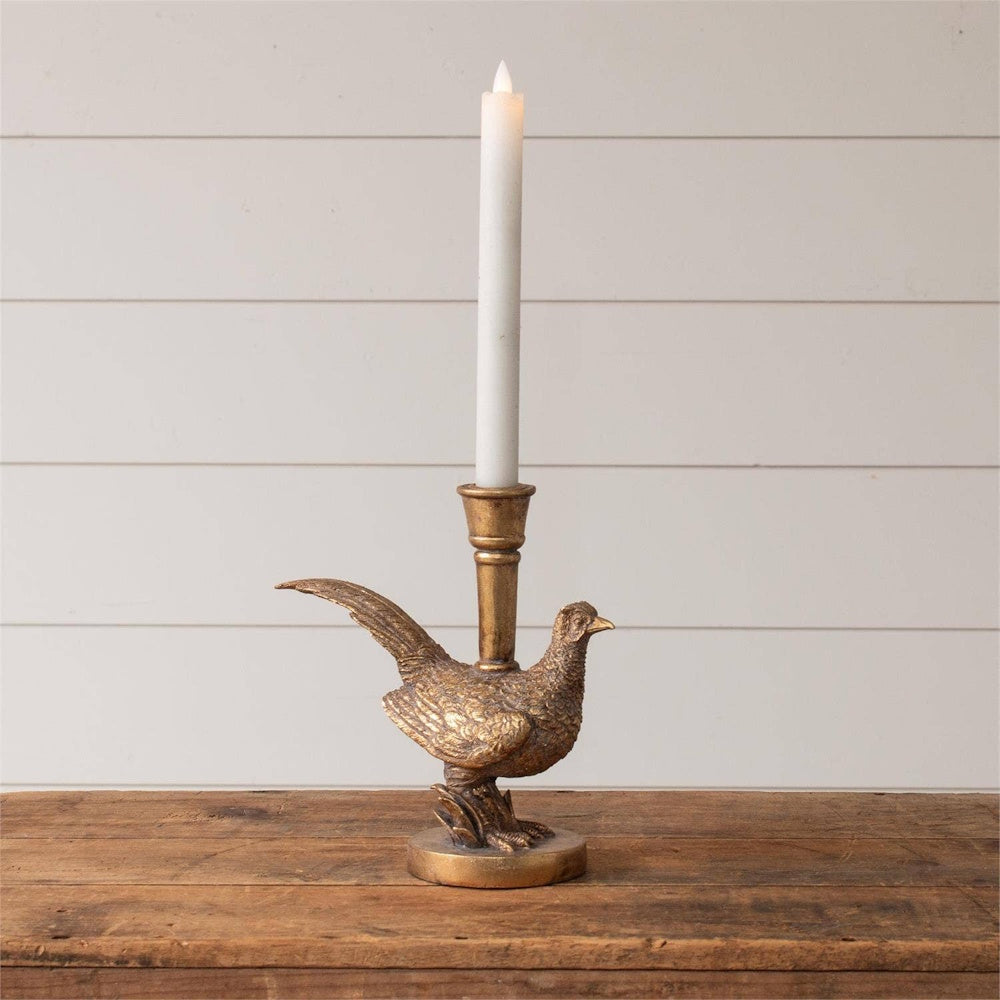 A gold-tone pheasant candleholder with a tall white taper candle on a wooden table.