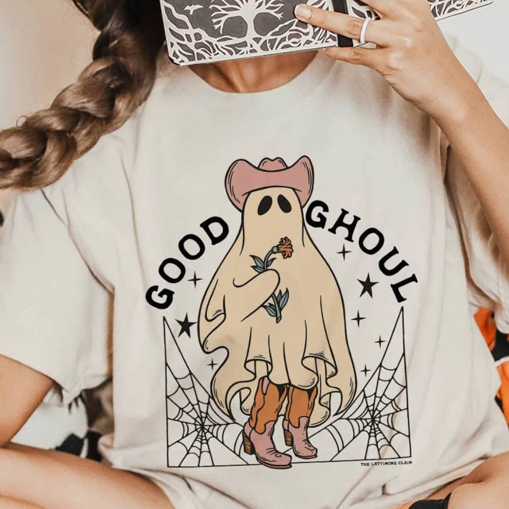 A beige graphic tee featuring a ghost wearing a pink cowboy hat and boots, with the words "GOOD GHOUL."