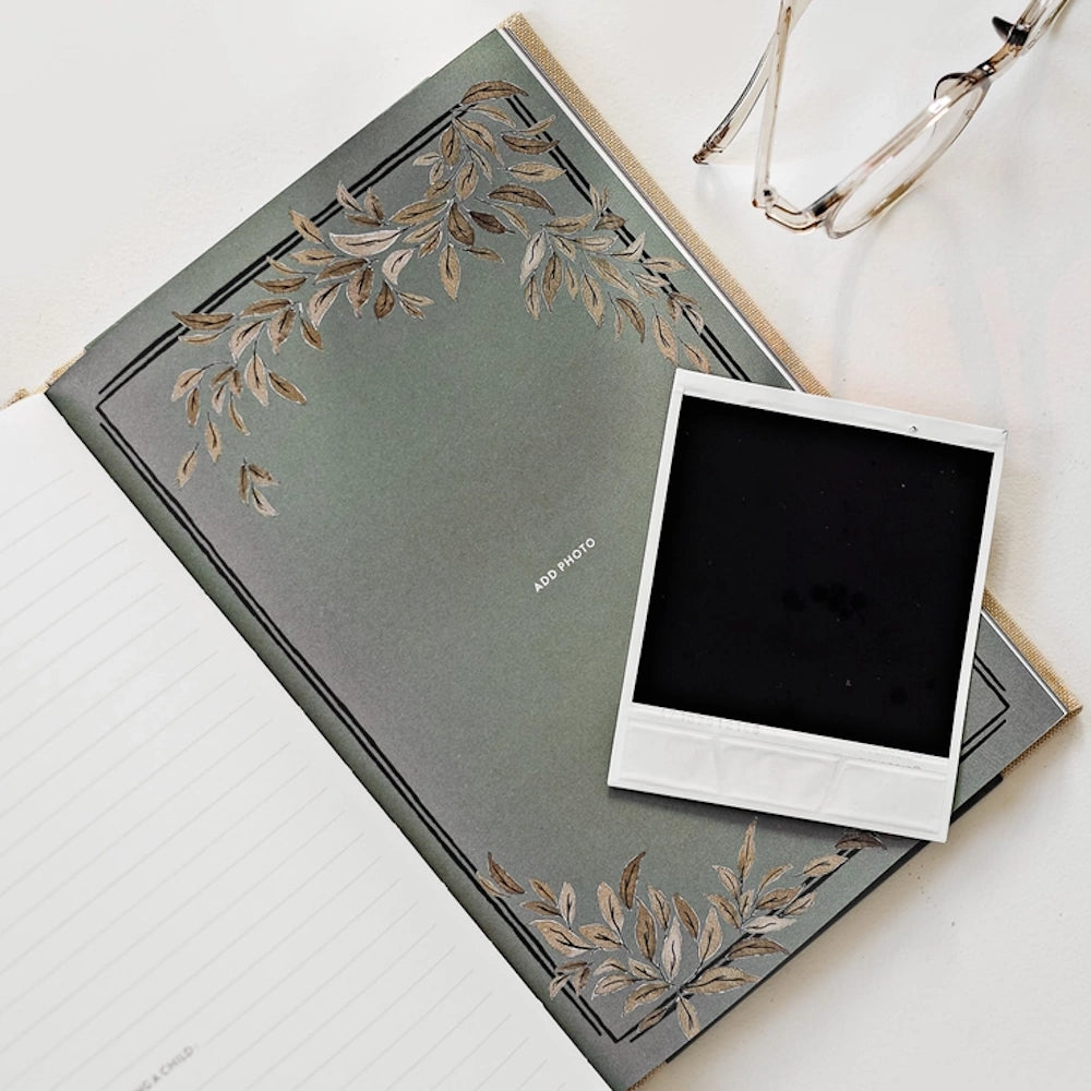 Open memory journal page with leaf illustrations and an instant film photo frame next to a pair of glasses.