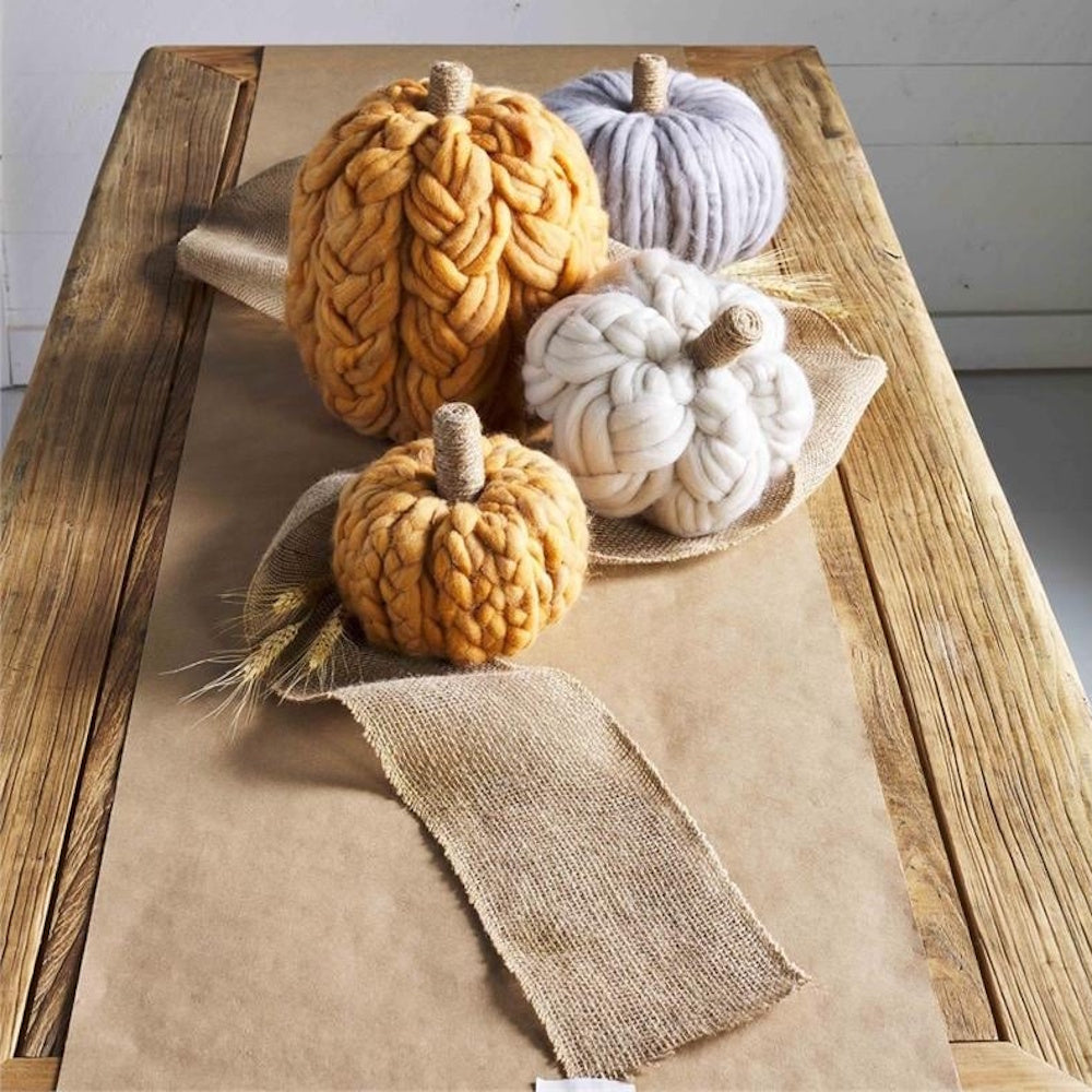Four chunky yarn-knit decorative pumpkins arranged on a rustic wooden table with burlap.