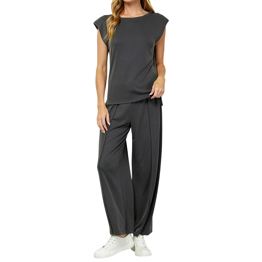 Woman wearing a dark gray padded-shoulder sleeveless top and matching wide-leg pants with white sneakers.