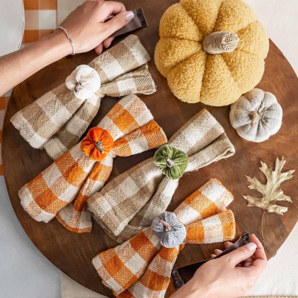 Autumn table setting featuring plaid napkins with pumpkin napkin rings on a round wooden tray.