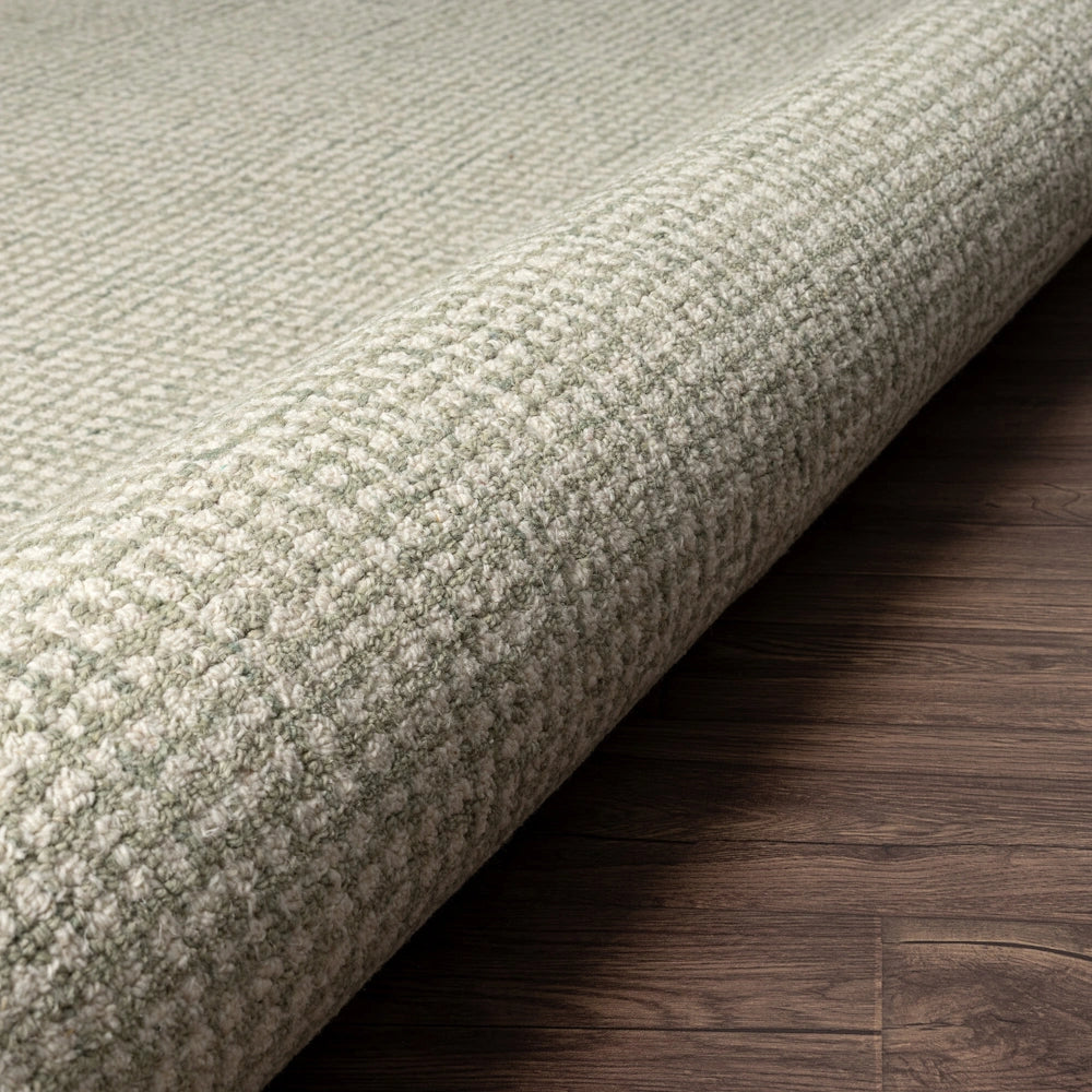 Textured light green wool rug with a loop pile weave rolled on a dark wood floor.