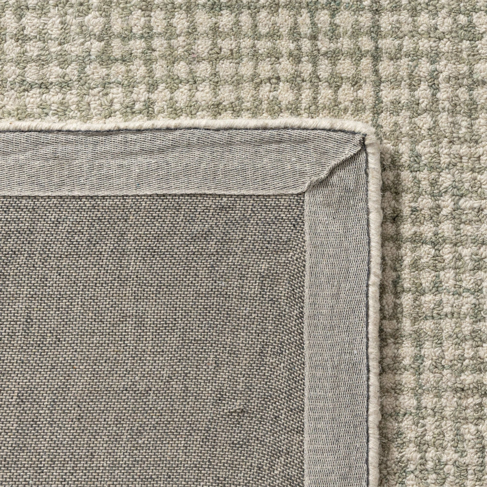 Close-up of the corner and non-slip backing of a sage green textured wool area rug with a grid pattern.