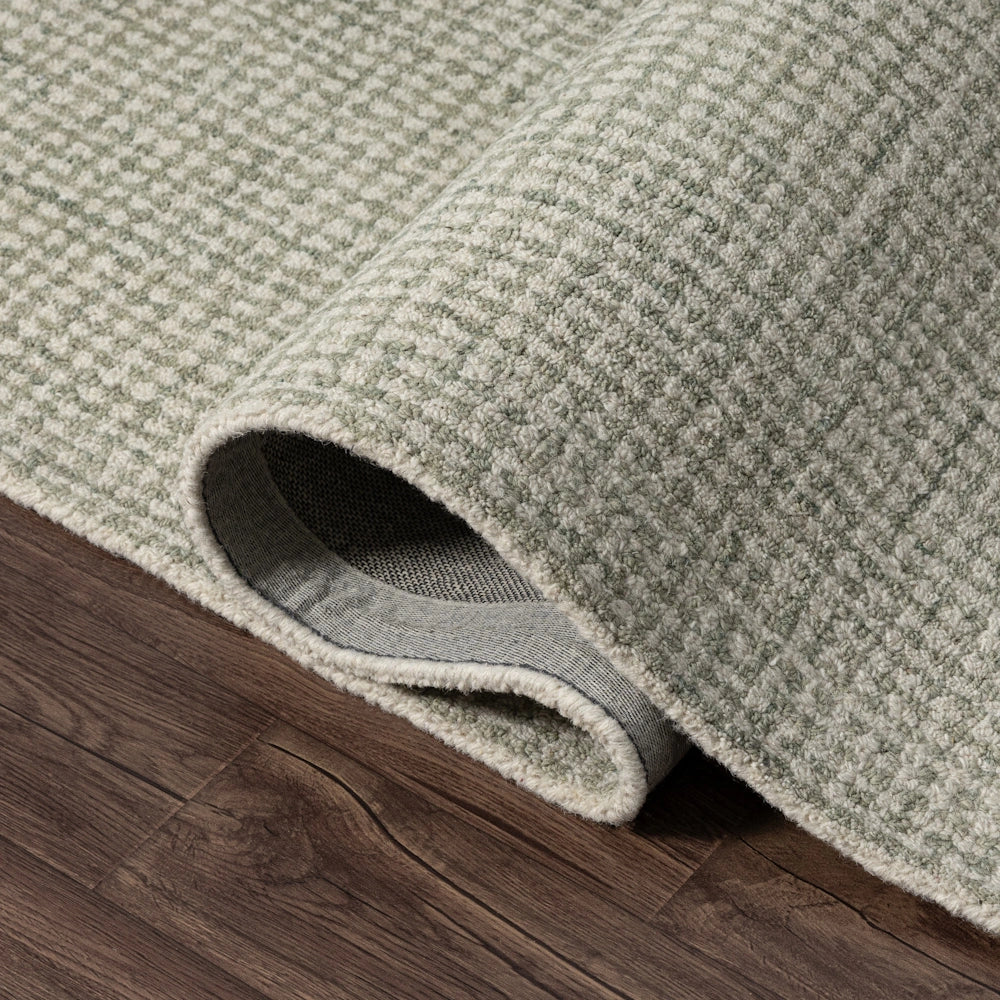 Sage green and cream textured wool area rug with a checkered weave pattern on dark wood flooring.