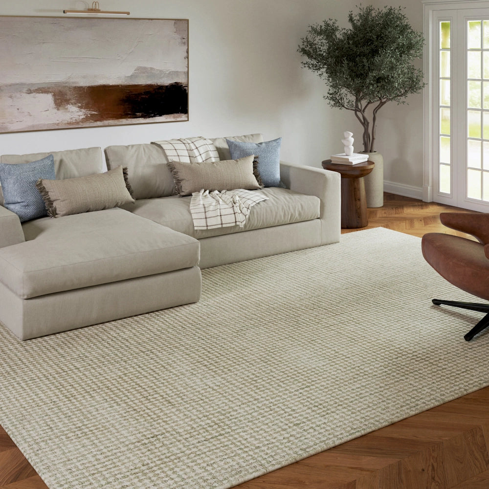 Modern living room with a beige sectional sofa, patterned area rug, and indoor olive tree on hardwood floors.