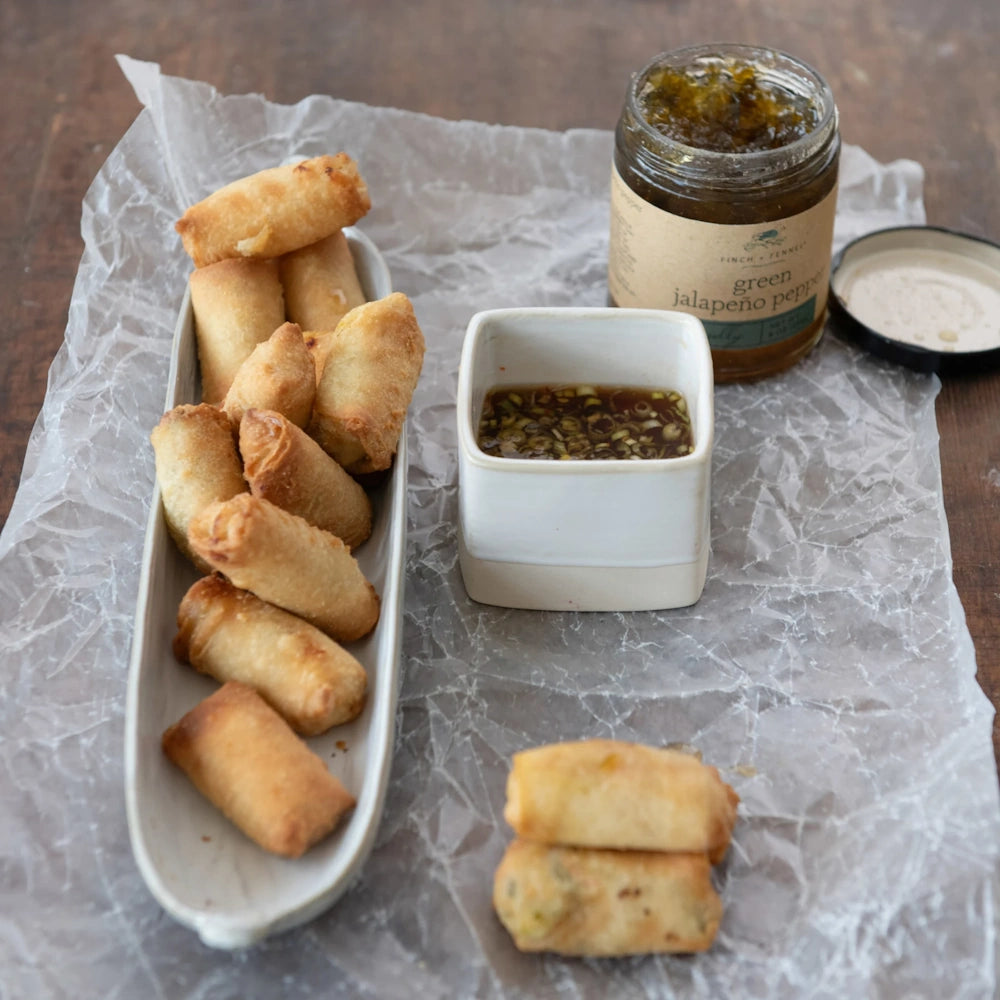 Crispy spring rolls served with dipping sauce beside an open jar of Finch + Fennel Green Jalapeño Pepper Jelly.
