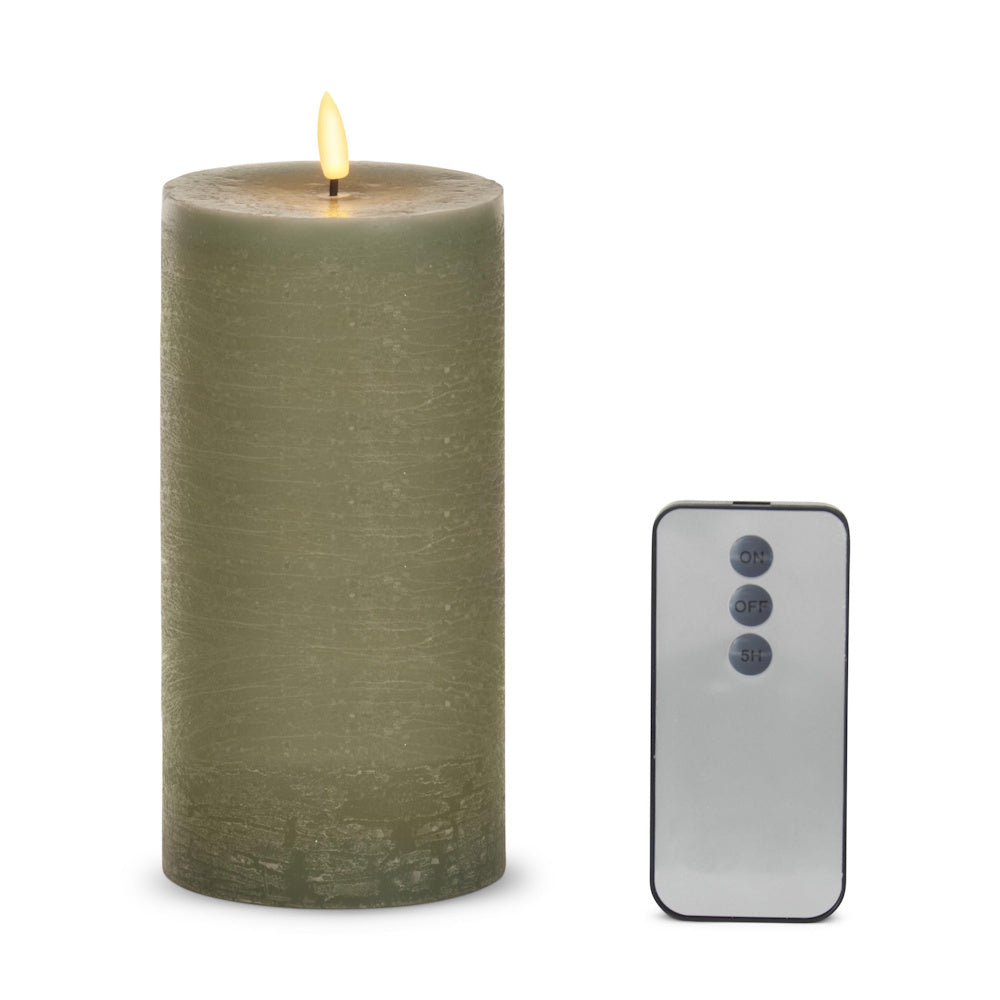 Sage green LED wax pillar candle with a lit flame next to a small gray remote with three buttons on a white background.