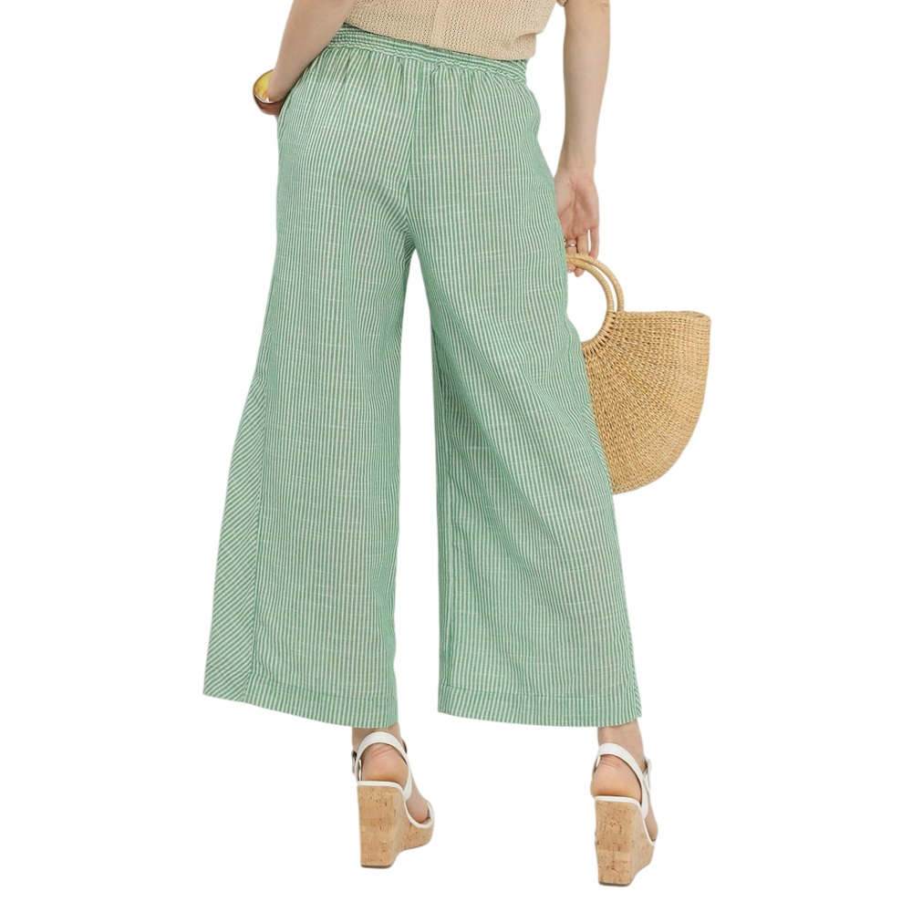 Back view of a person wearing green and white striped wide-leg pants, platform sandals, and holding a straw bag.