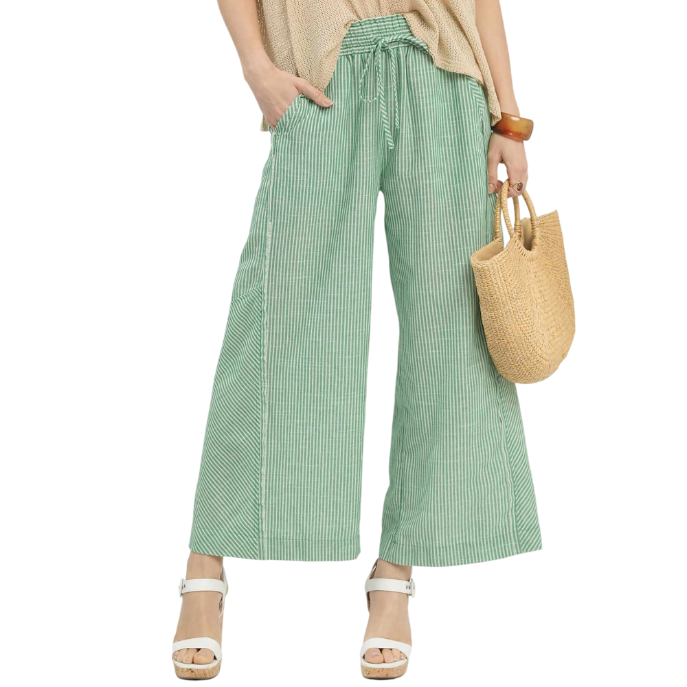 A person wearing green and white striped wide-leg pants with a drawstring waist and white wedge sandals.