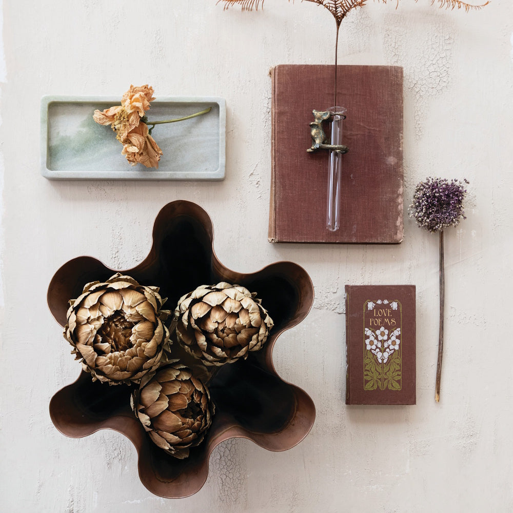 Flat lay of a green marble tray, vintage books, dried flowers, and artichokes in a wavy bowl.