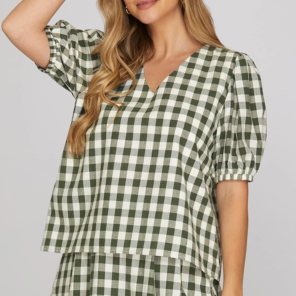 Front view of a woman wearing a green and white gingham checked v-neck top with short puff sleeves.