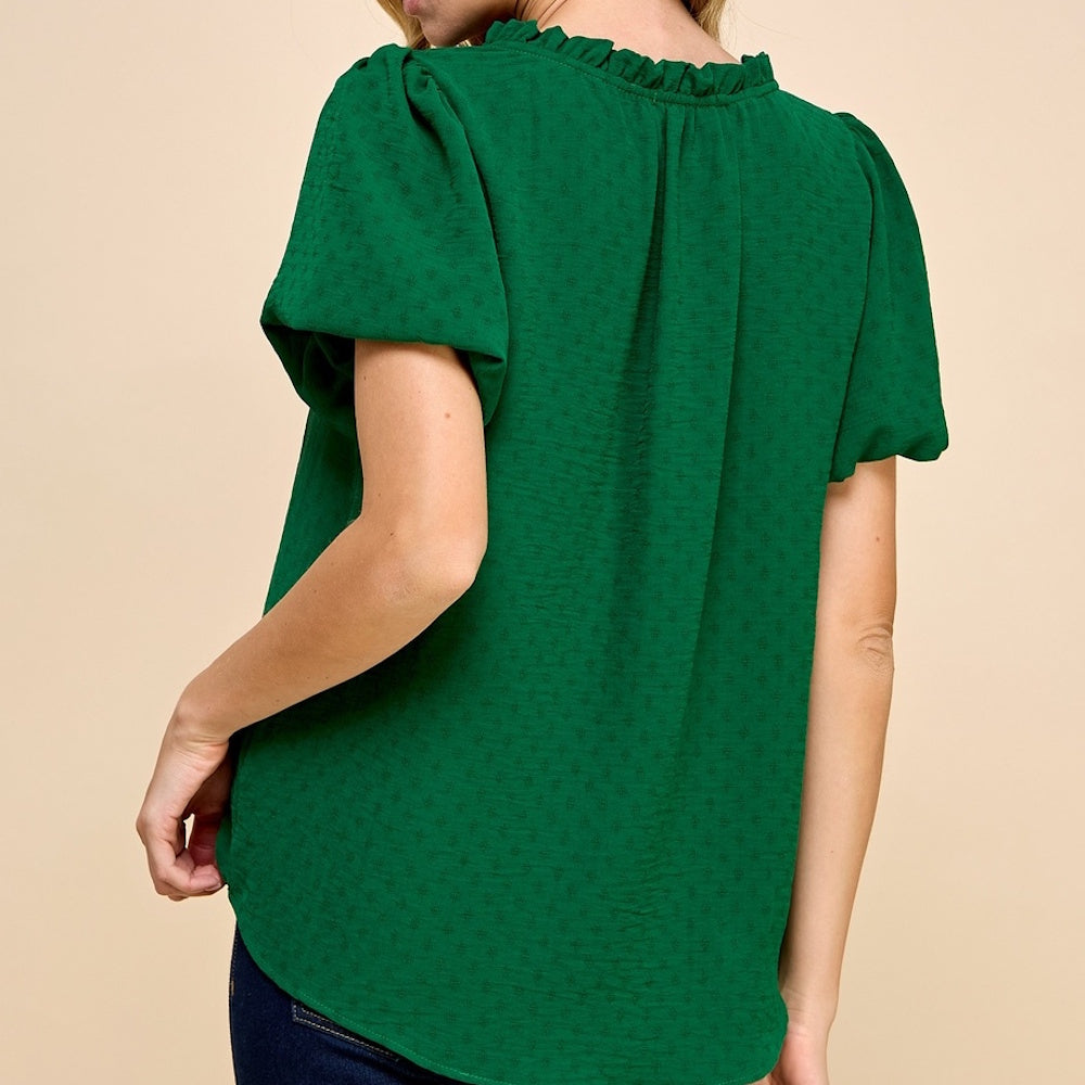 Rear view of a person wearing a textured emerald green blouse with short puff sleeves and a ruffled neckline.