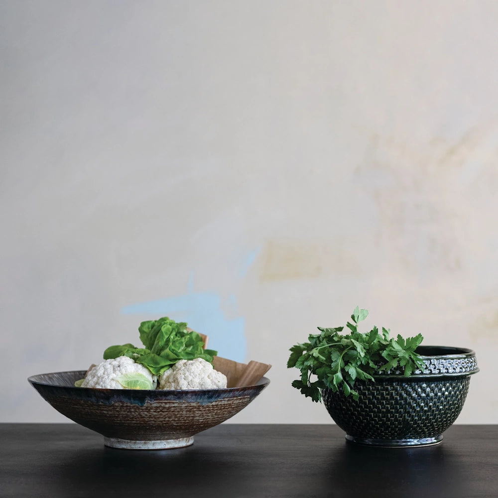 Green stoneware basket weave bowl with fresh parsley next to a ceramic bowl of cauliflower on a dark table.