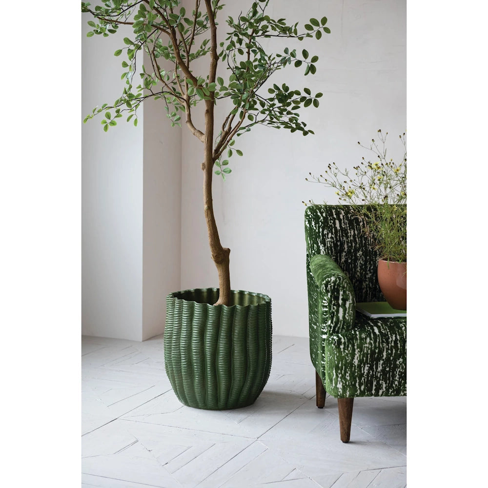 Green fluted stoneware planter with a large indoor tree next to a patterned green armchair in a bright room.