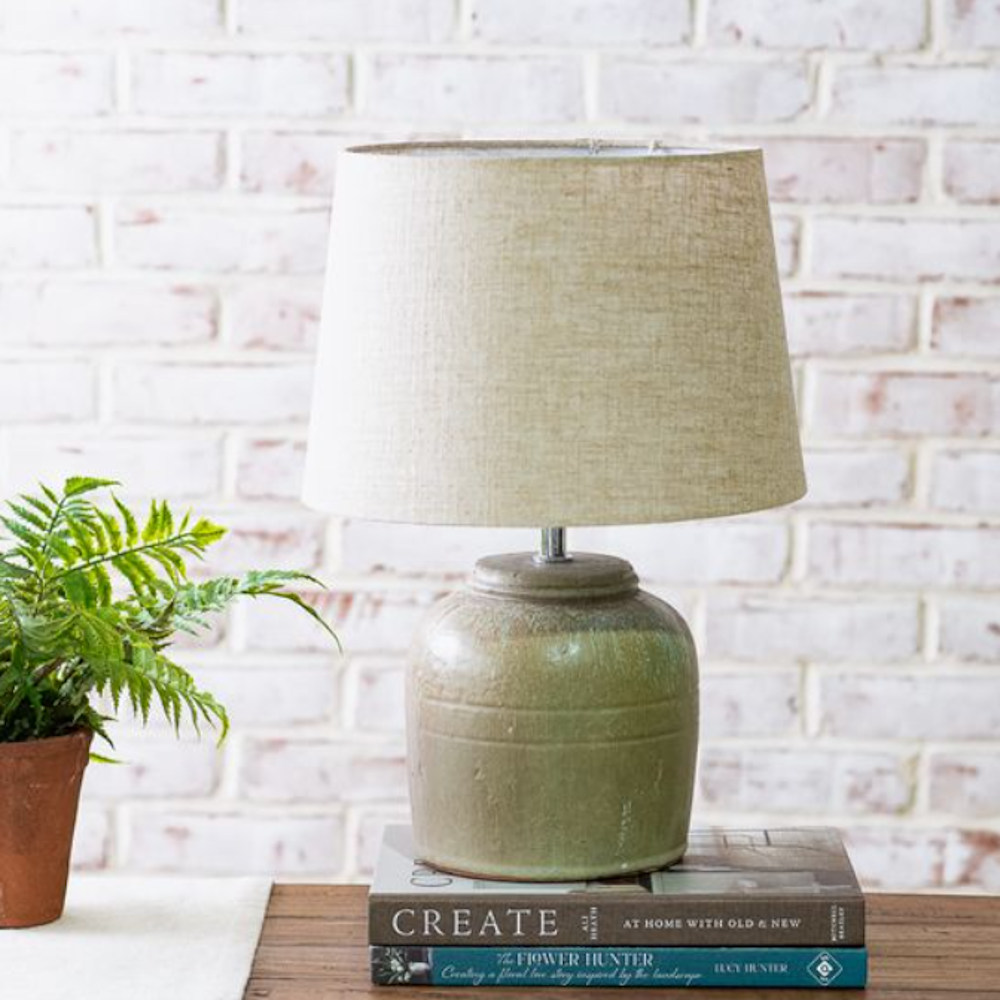 Green textured terracotta table lamp with a linen shade sitting on stacked books.