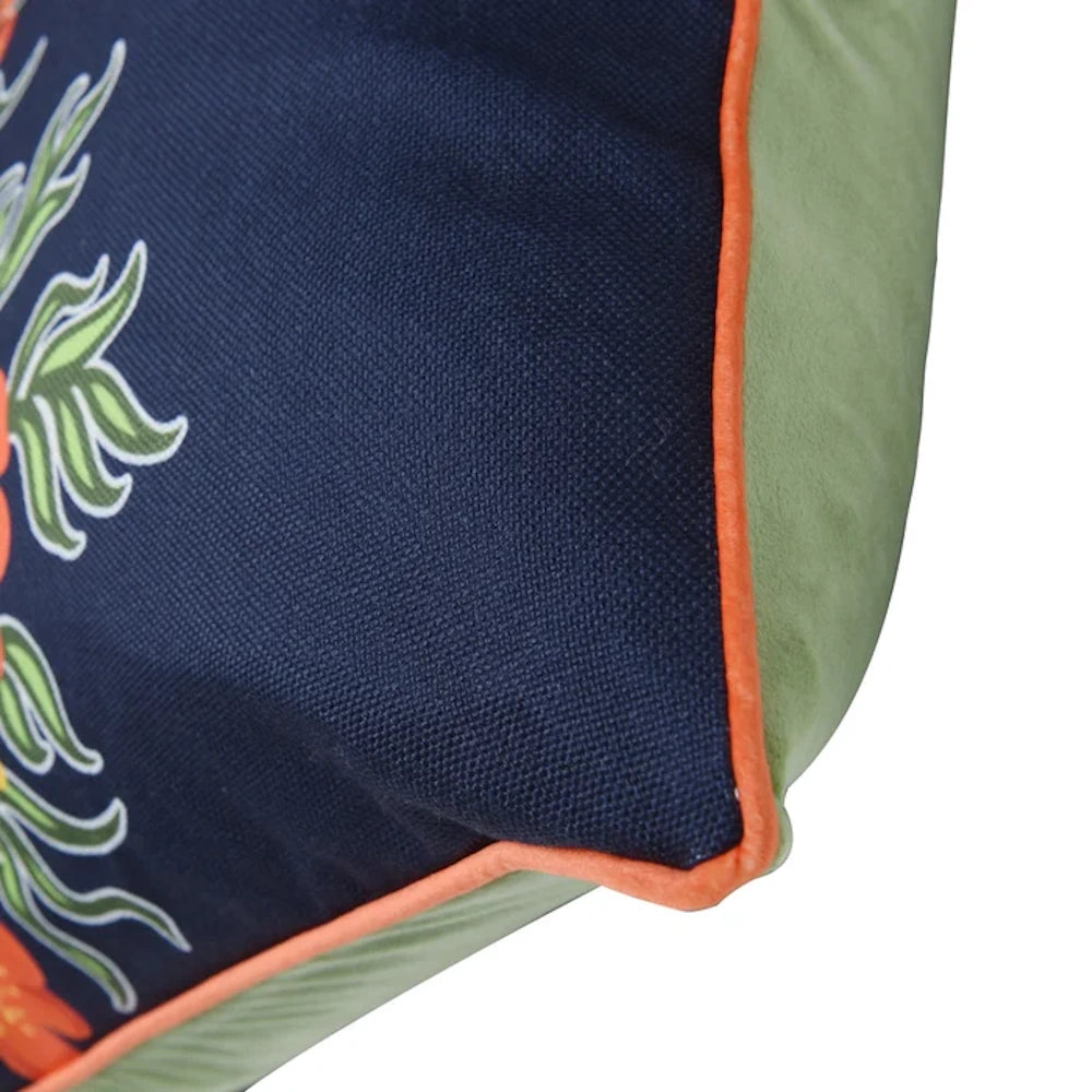 Close-up of a navy blue canvas pillow with orange piping and a green velvet back, featuring a colorful floral pattern.