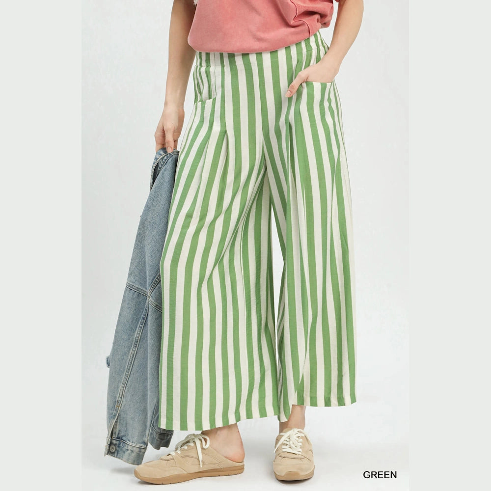 Woman wearing green and white vertical striped wide-leg pants with a pink shirt, denim jacket, and beige sneakers.